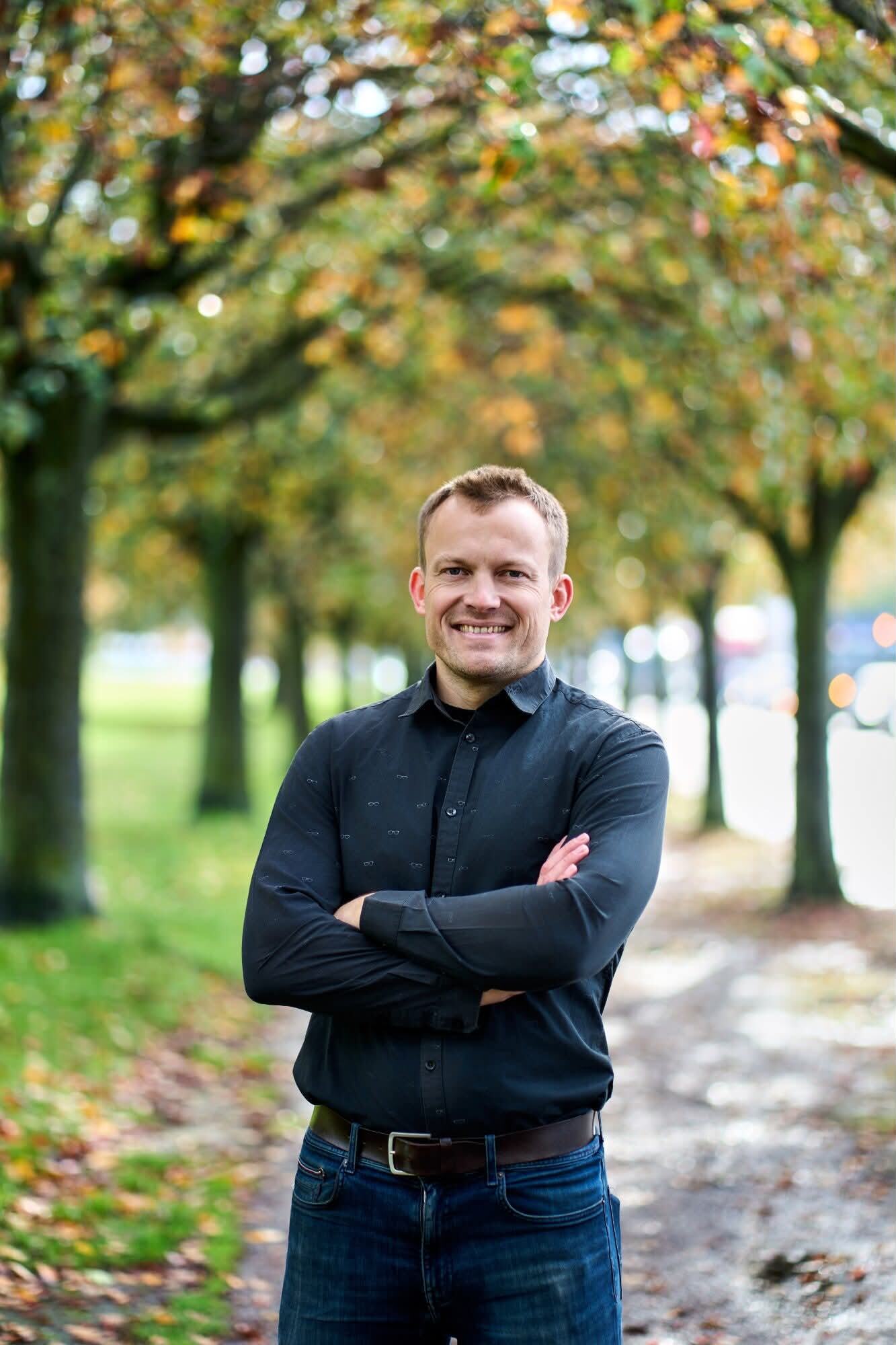 Psykoterapeut Thomas Jørgensen smiler med armene over kors i en efterårsallé